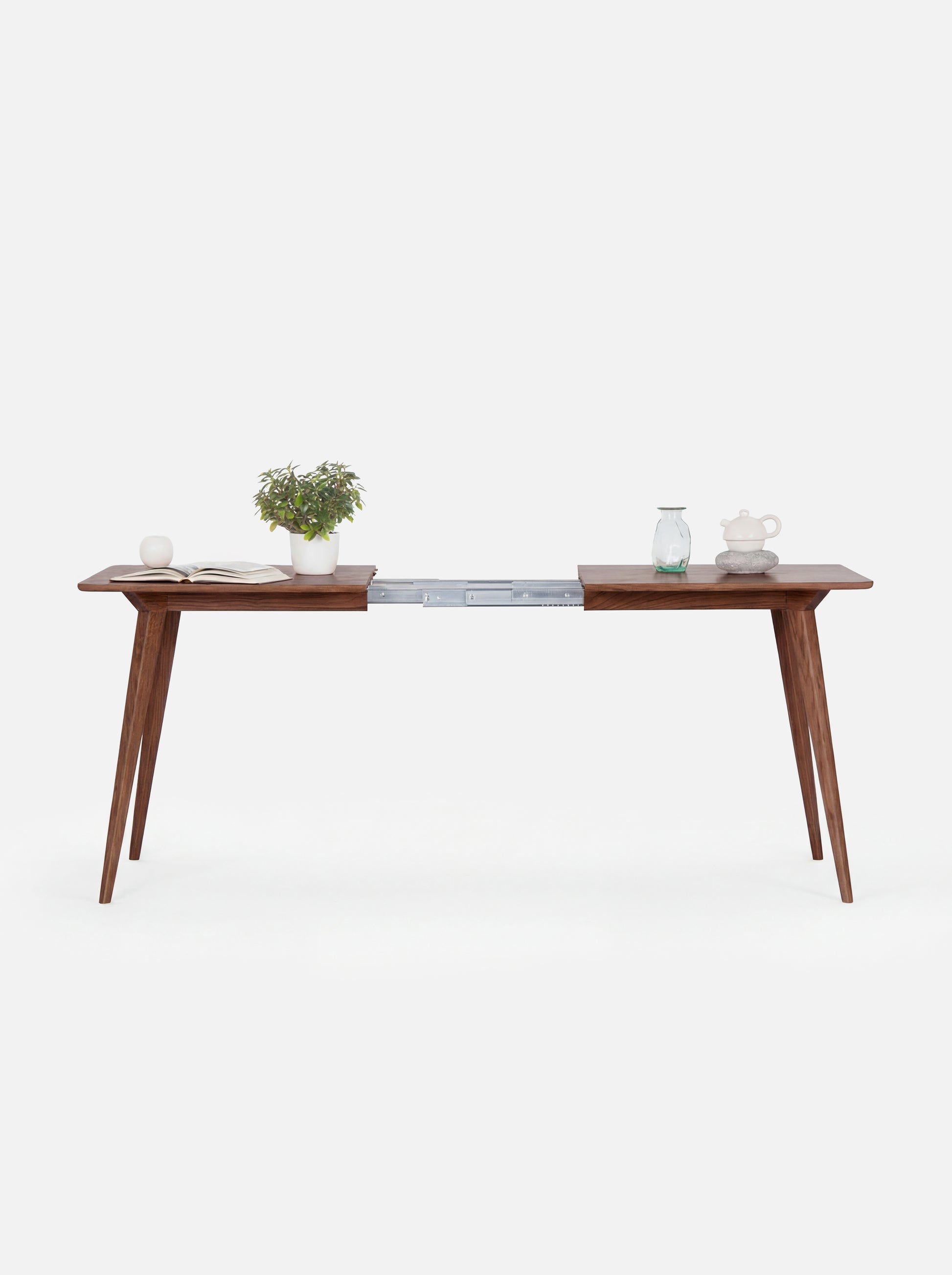 Minimalist wooden desk with tapered legs, featuring plants and ceramic items.