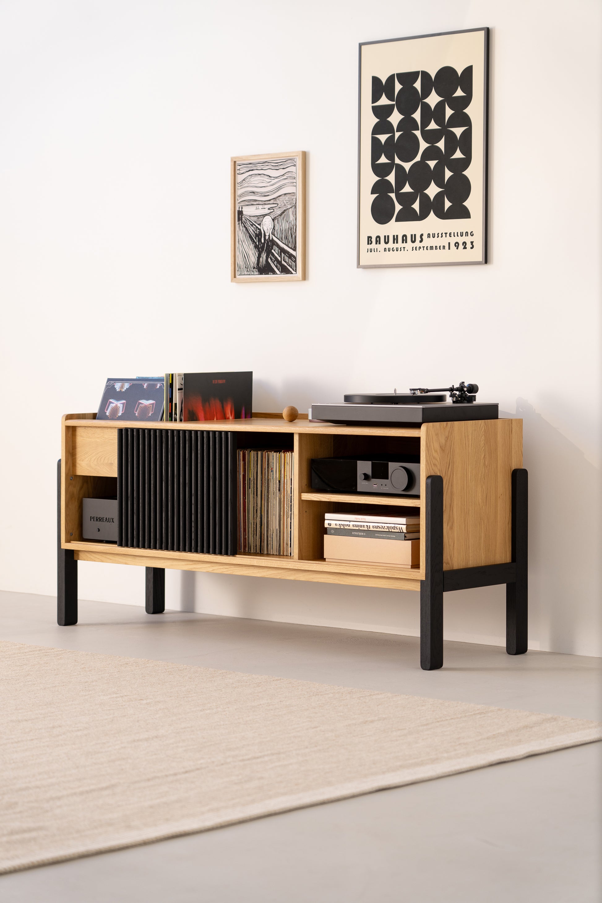 Modern wooden sideboard with a turntable and records, beneath framed posters on a light wall.