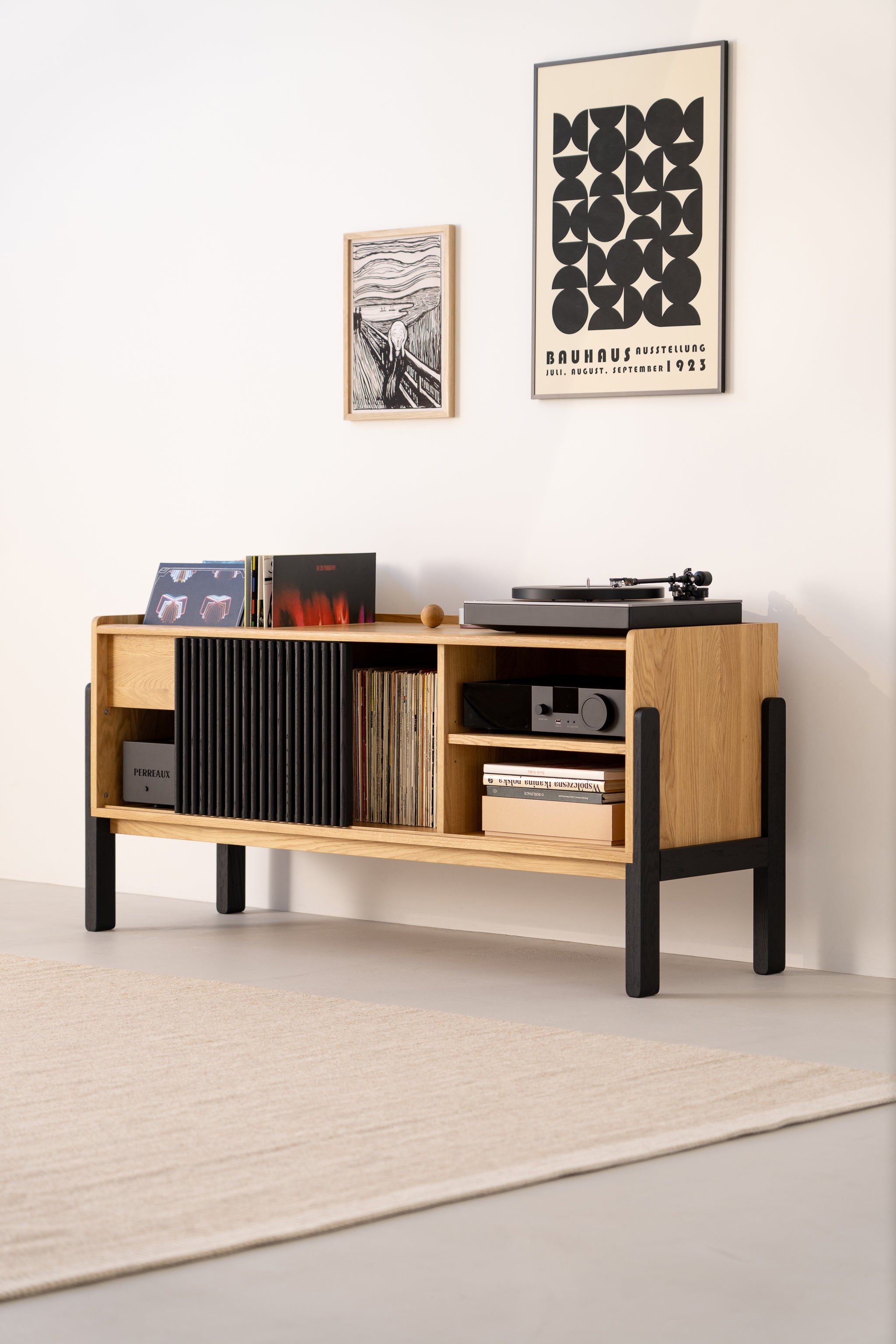 Modern wooden sideboard with a turntable and records, beneath framed posters on a light wall.