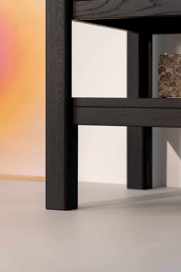 Close-up of a dark wood table leg on a light surface with a blurred colorful background.