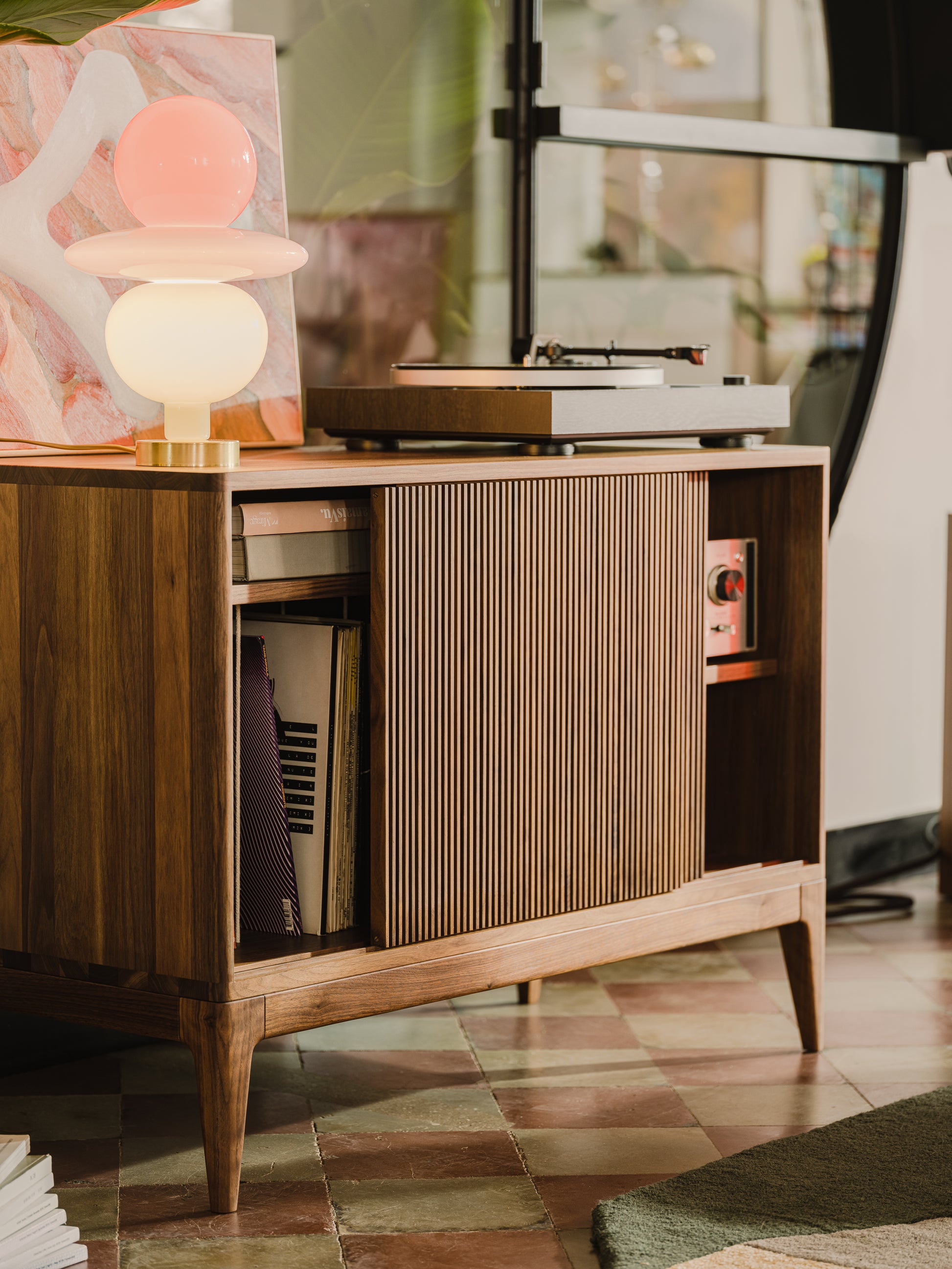 Mid-century wooden console with a record player, colorful lamp, and vinyl records on tiled floor.