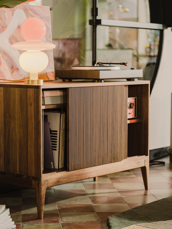 Mid-century wooden console with a record player, colorful lamp, and vinyl records on tiled floor.