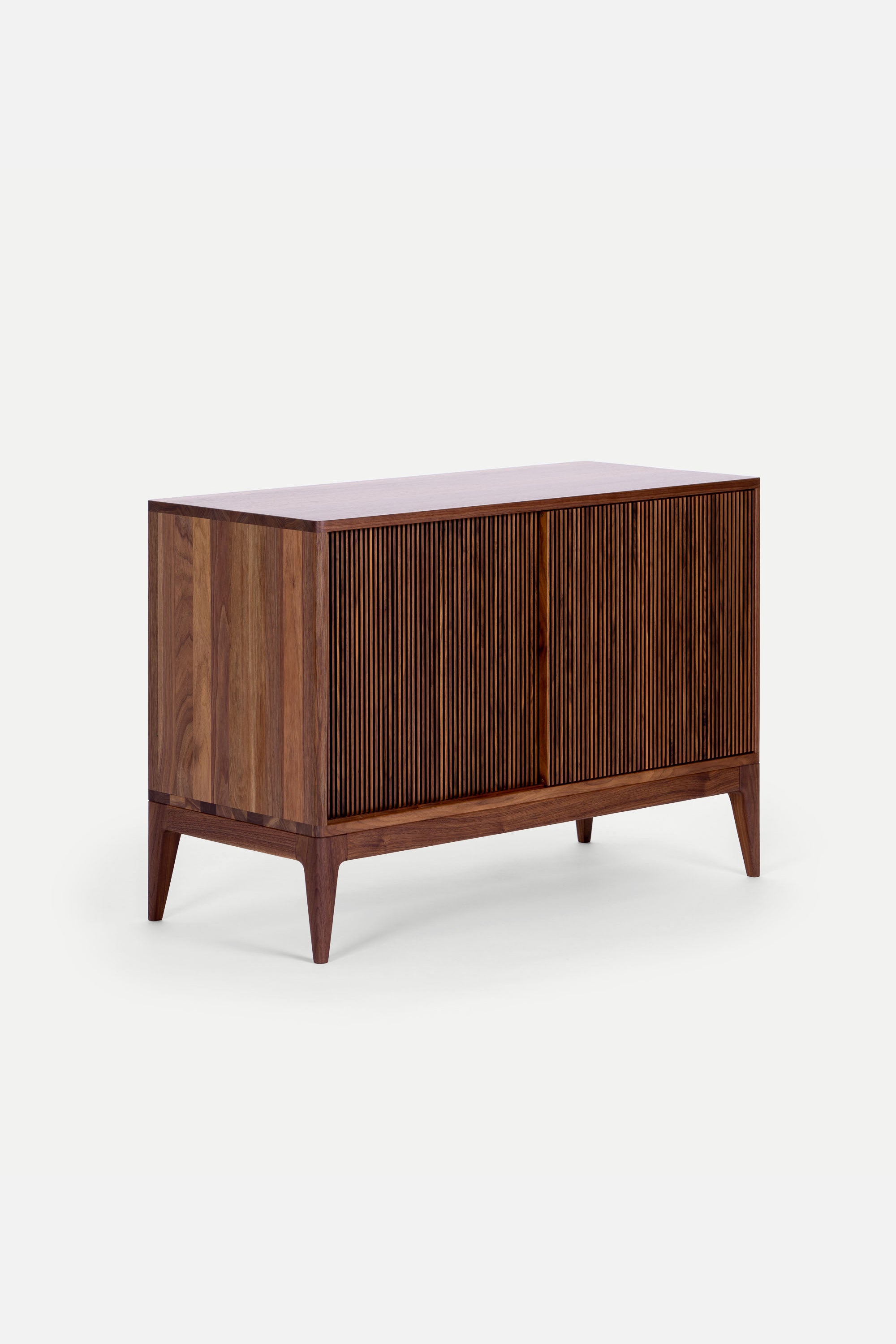 Wooden chest of drawers with a ribbed front design and tapered legs against a white background.