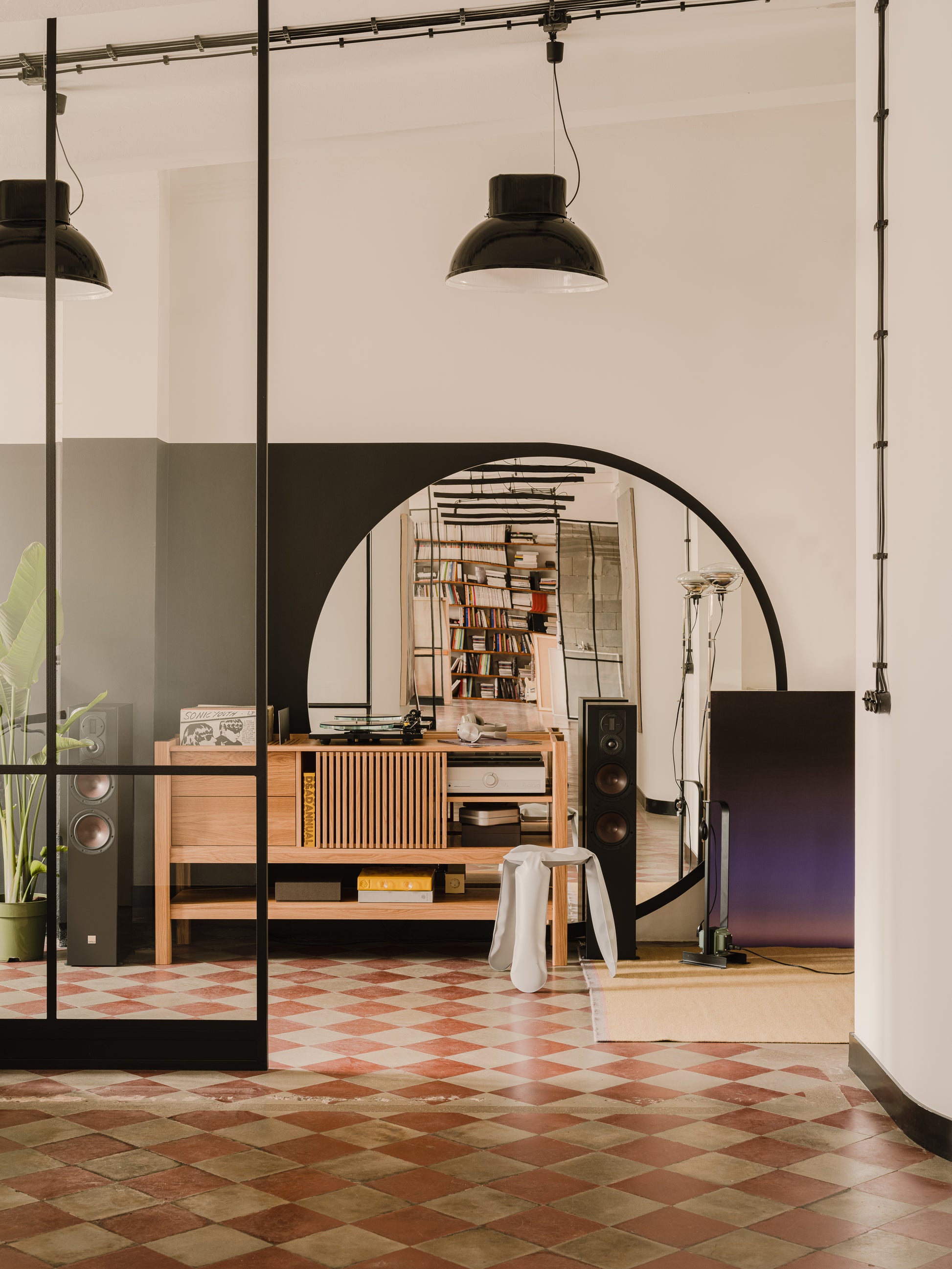 Modern room with checkered floor, wooden furniture, large mirror, and speakers. Pendant lights hang from the ceiling.