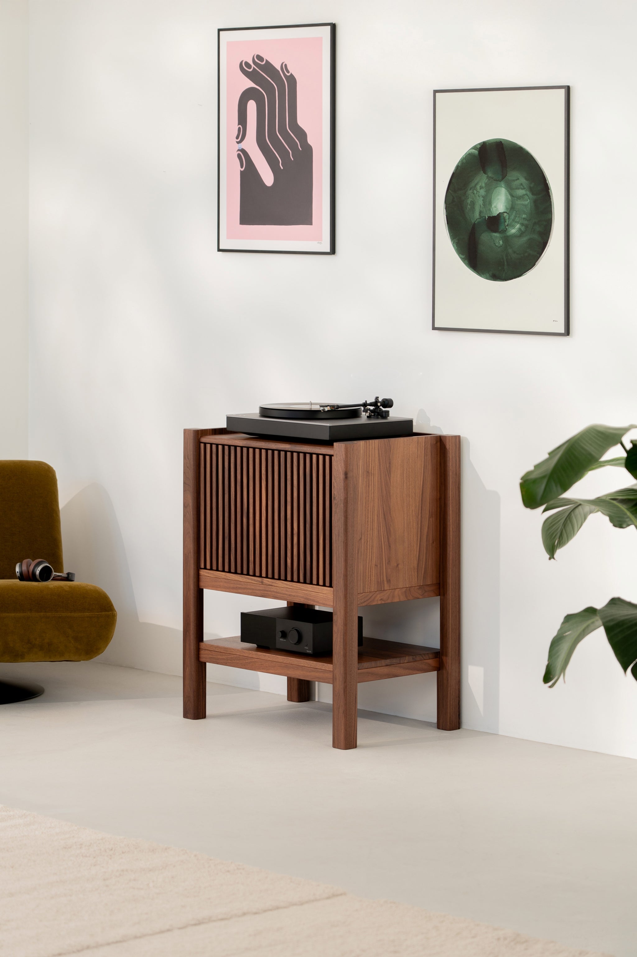 Mid-century modern audio setup with a turntable, wooden cabinet, artworks, chair, and plant.
