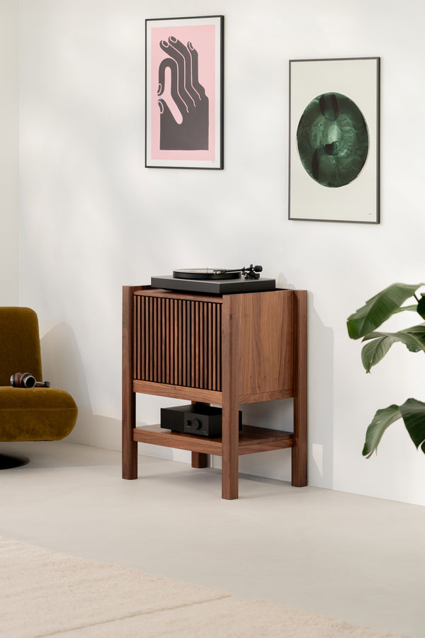 Mid-century modern audio setup with a turntable, wooden cabinet, artworks, chair, and plant.