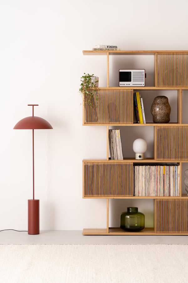 Minimal room with a wooden shelf, books, and a red floor lamp against a white wall.