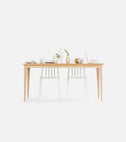 FARM solid oak farmhouse dining table, front view, two white spindle chairs behind it, vases, plates and a laptop on top