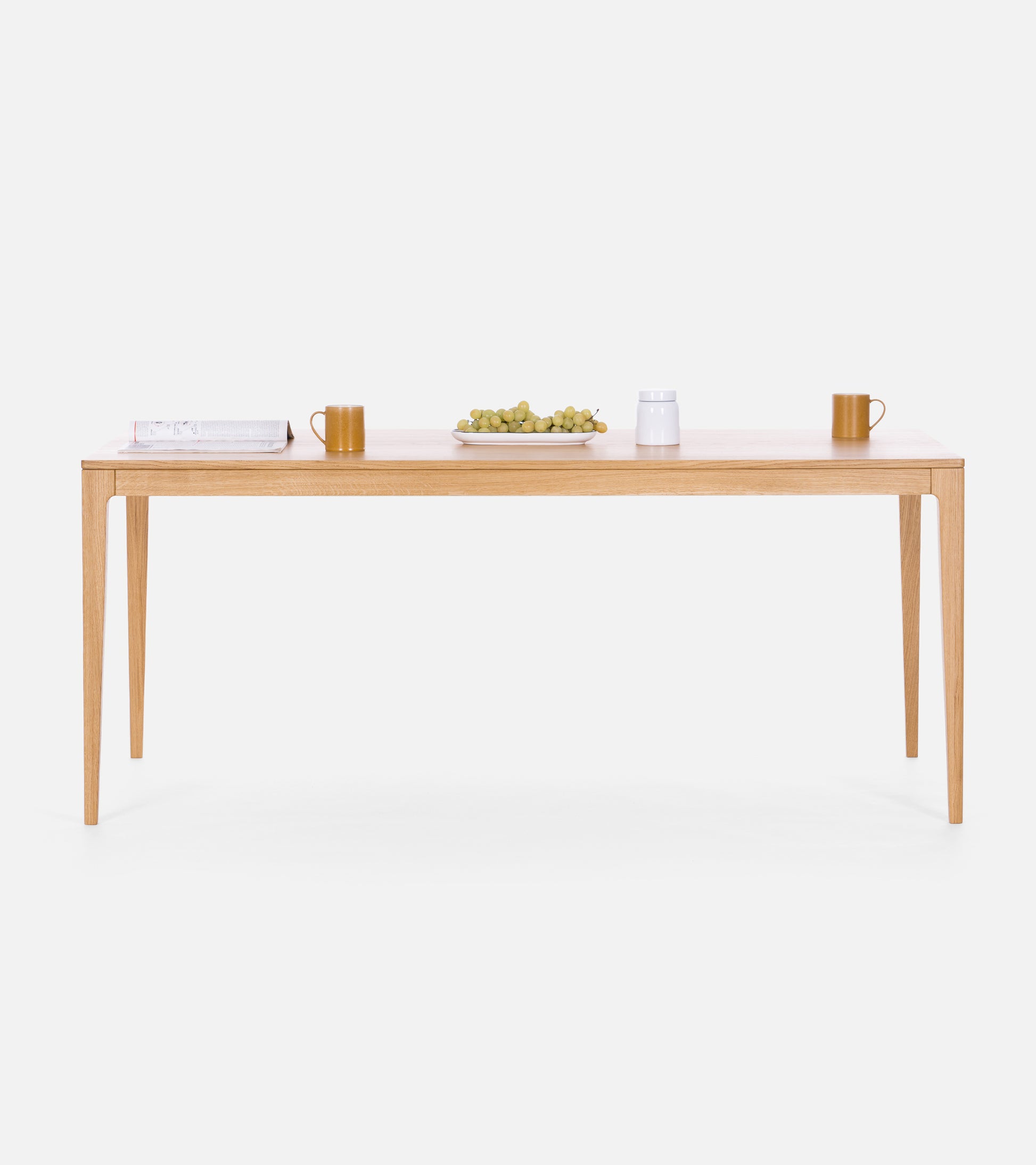 Minimalist wooden table with a book, two mugs, a plate of grapes, and a white jar.
