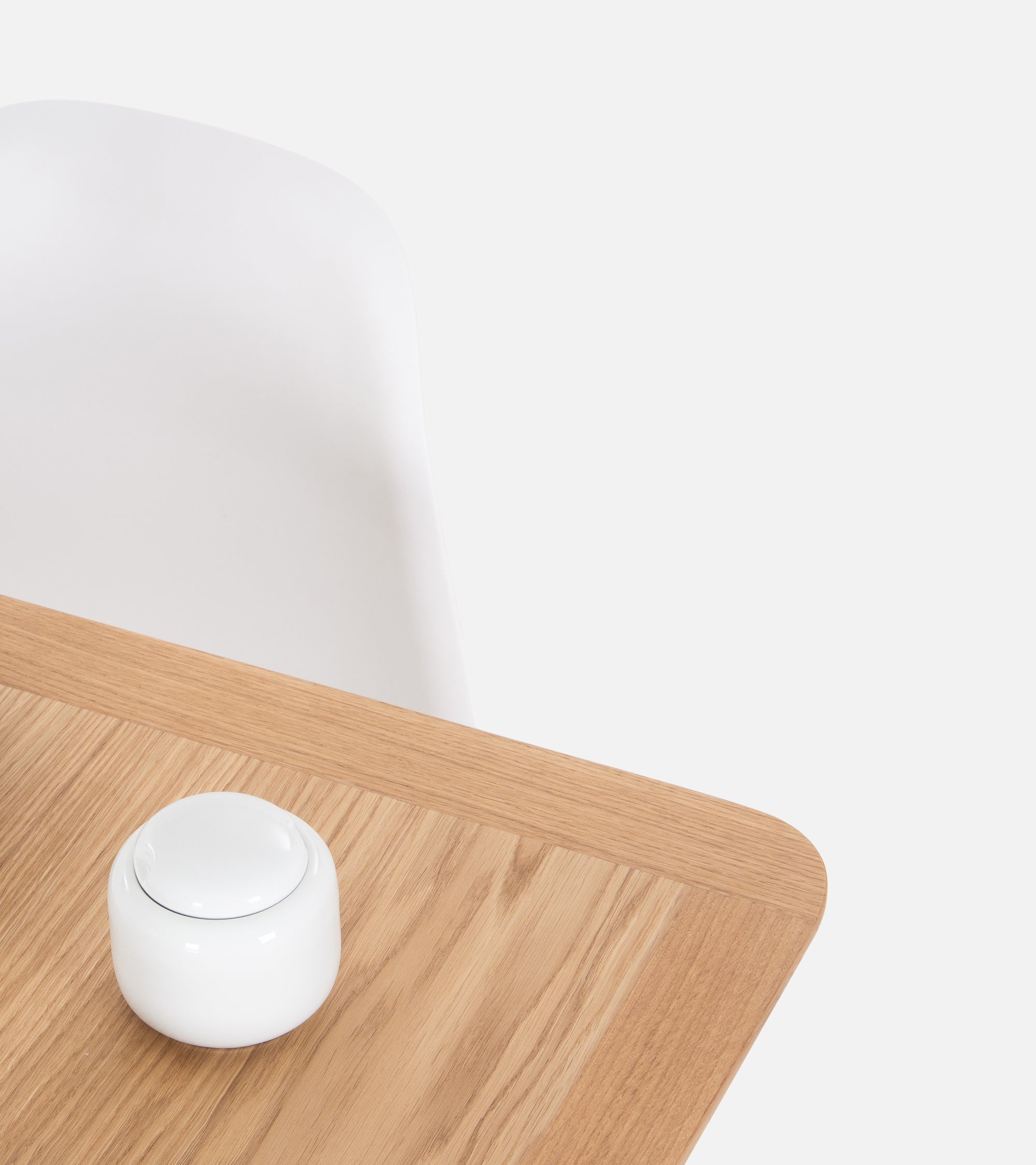 Minimalist wooden table with a small white container and a white chair in the background.