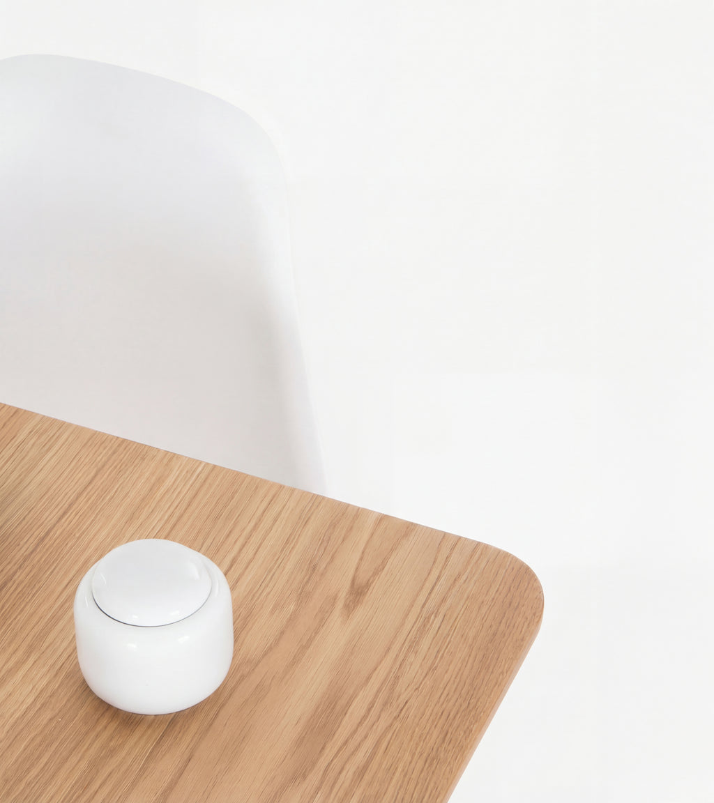 Minimalist wooden table with a small white container and a white chair in the background.