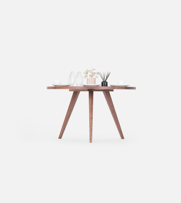 Minimalist wooden table set with white dishes, glasses, decorative hands, a small plant, and a black reed diffuser.