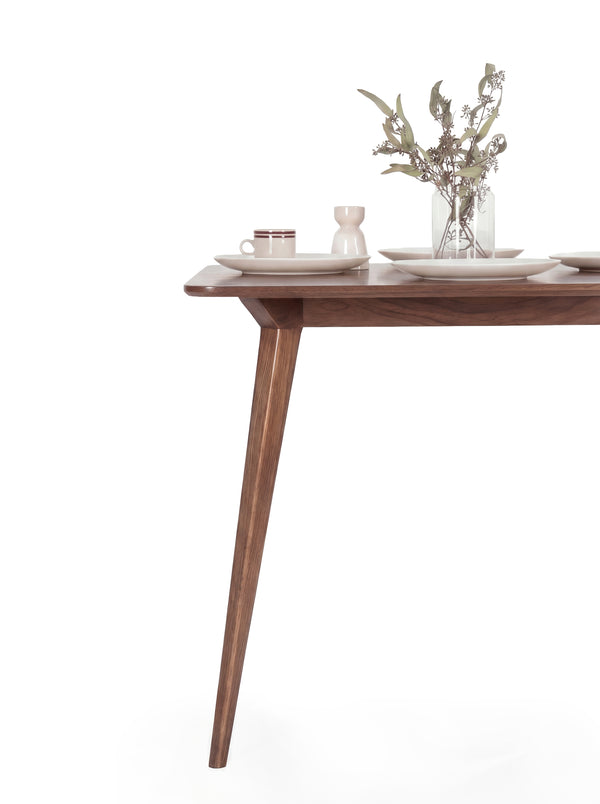 Modern wooden table with a cup, saucer, vase, and foliage centerpiece.