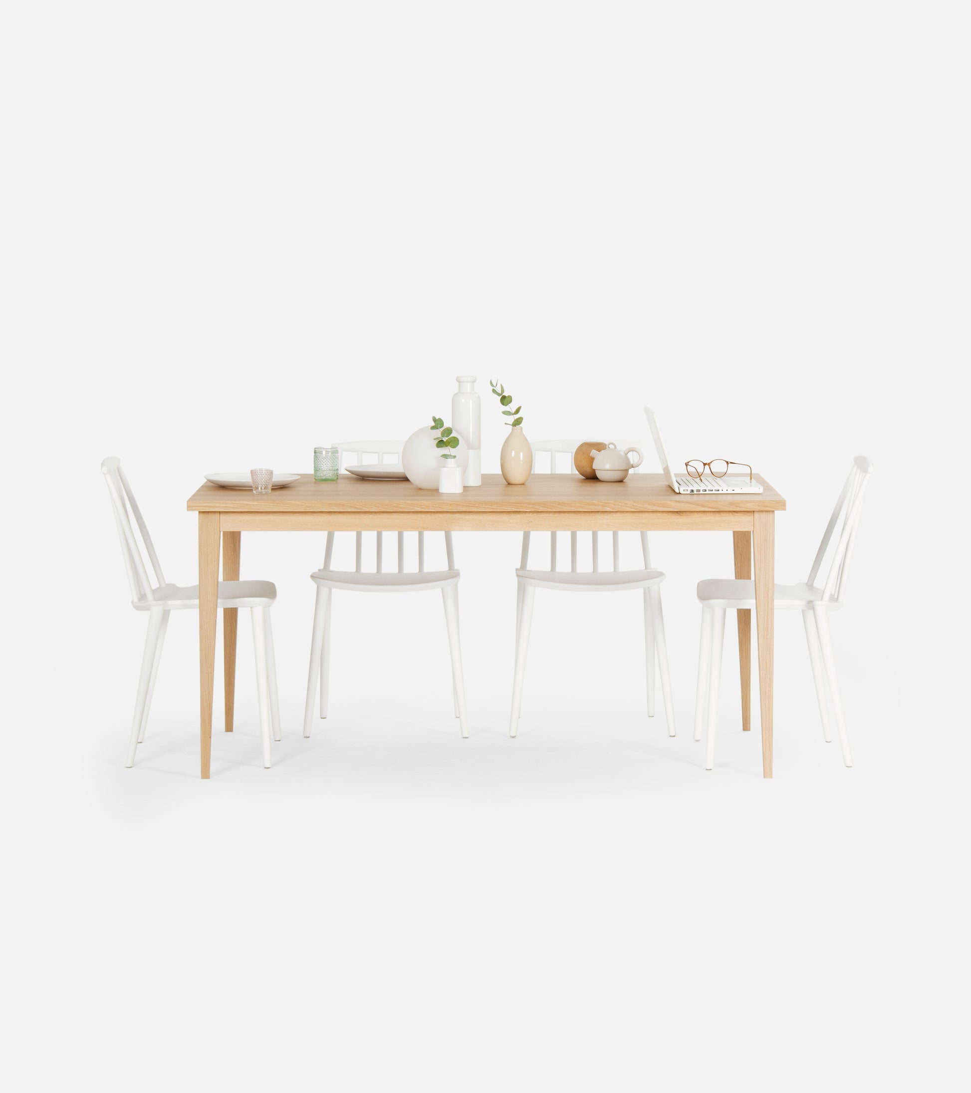 Minimalist dining table set with wooden table, white chairs, vases, laptop, and tableware.