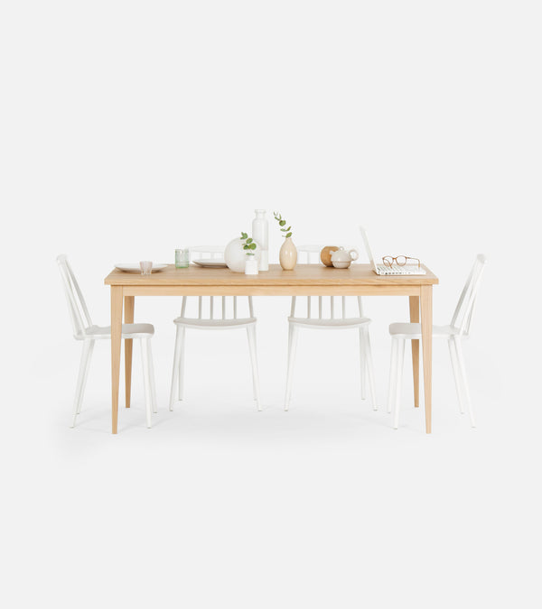 Minimalist dining table set with wooden table, white chairs, vases, laptop, and tableware.