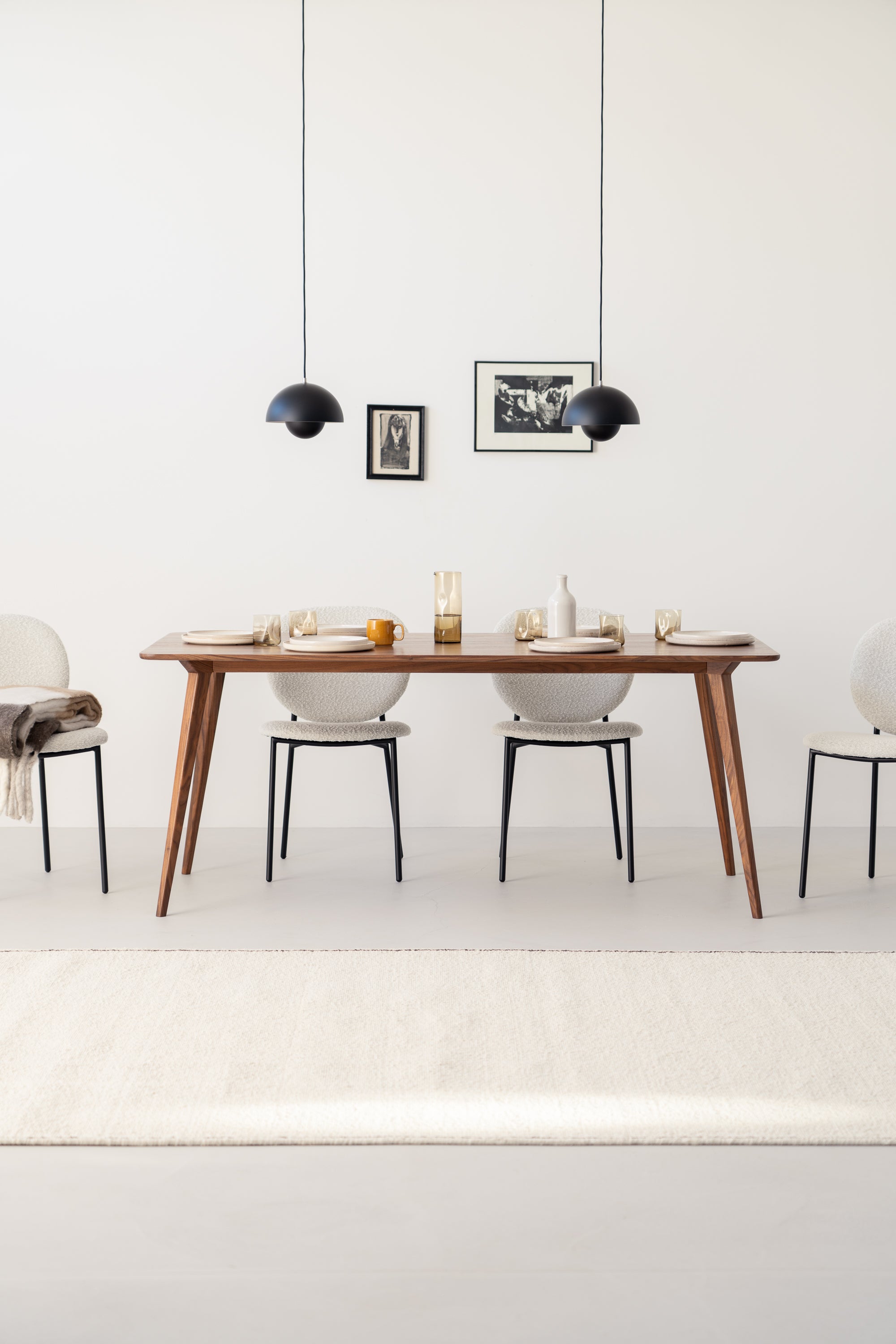 Modern dining room with a wooden table, minimal décor, four chairs, pendant lights, and framed wall art.