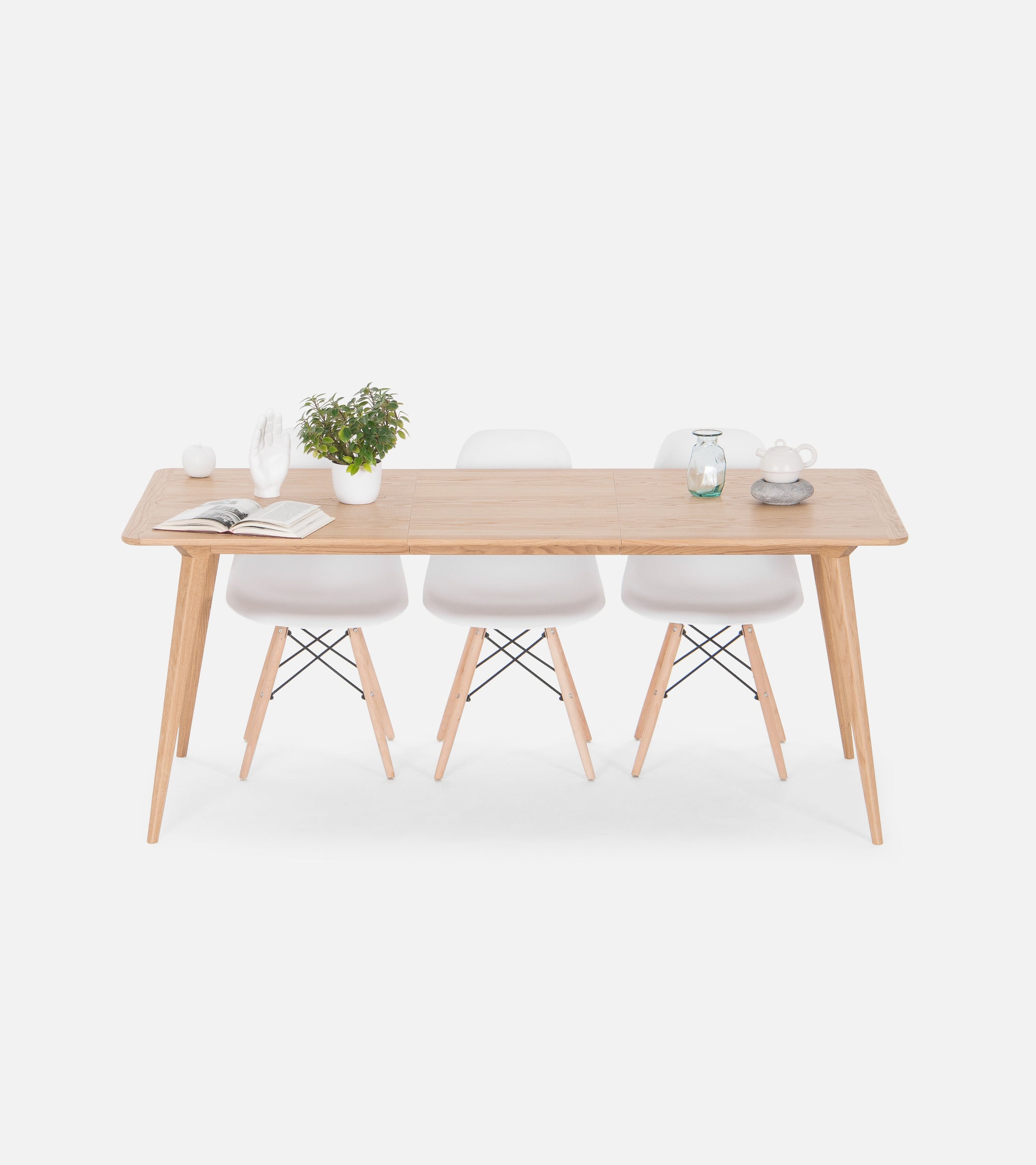 Minimalist wooden dining table with three white chairs, a plant, and decorative items.