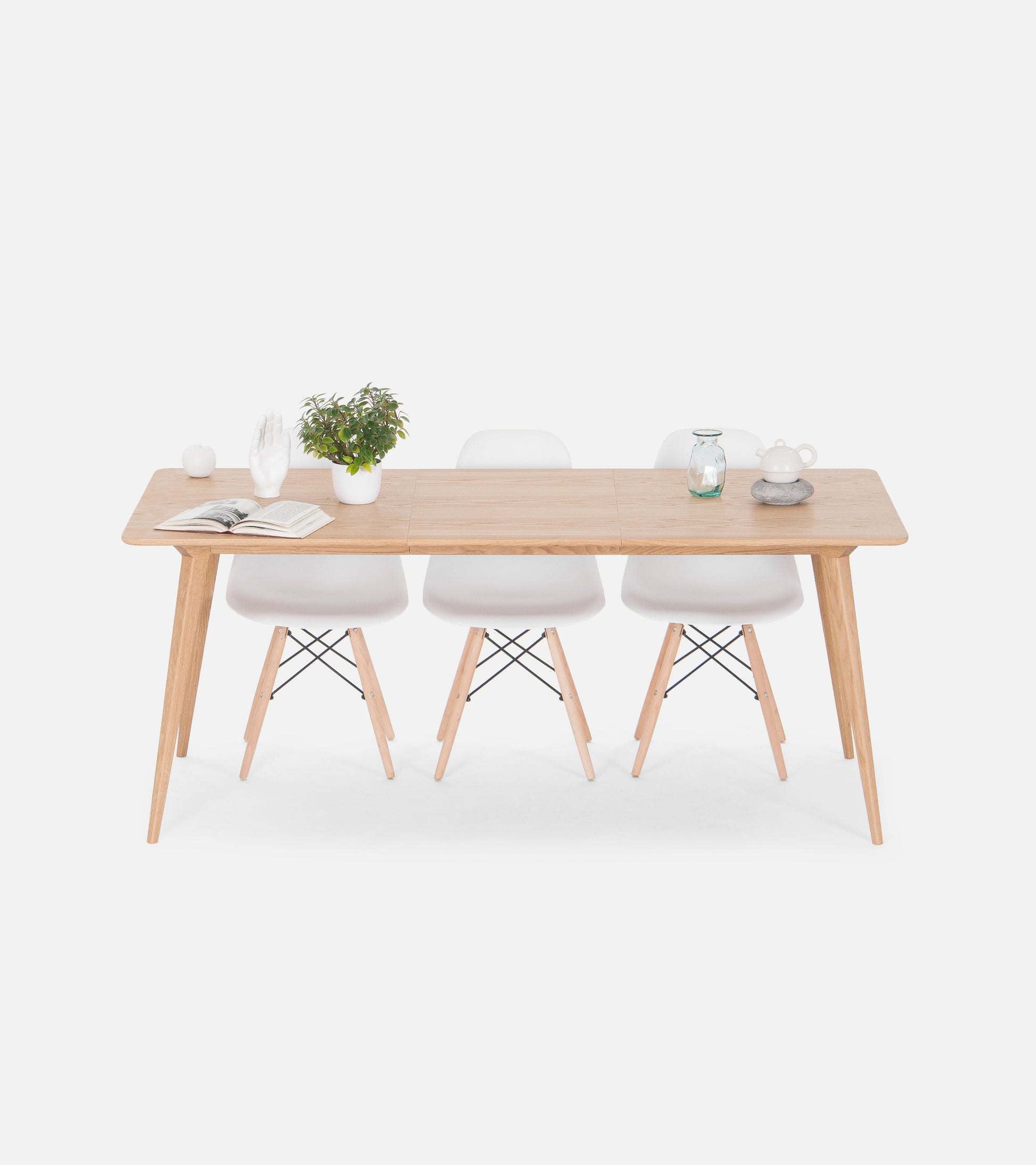 Minimalist wooden dining table with three white chairs, a plant, and decorative items.