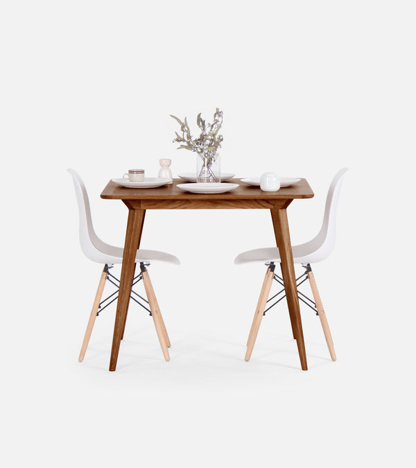 Minimalist dining setup with a wooden table, white chairs, and tableware.