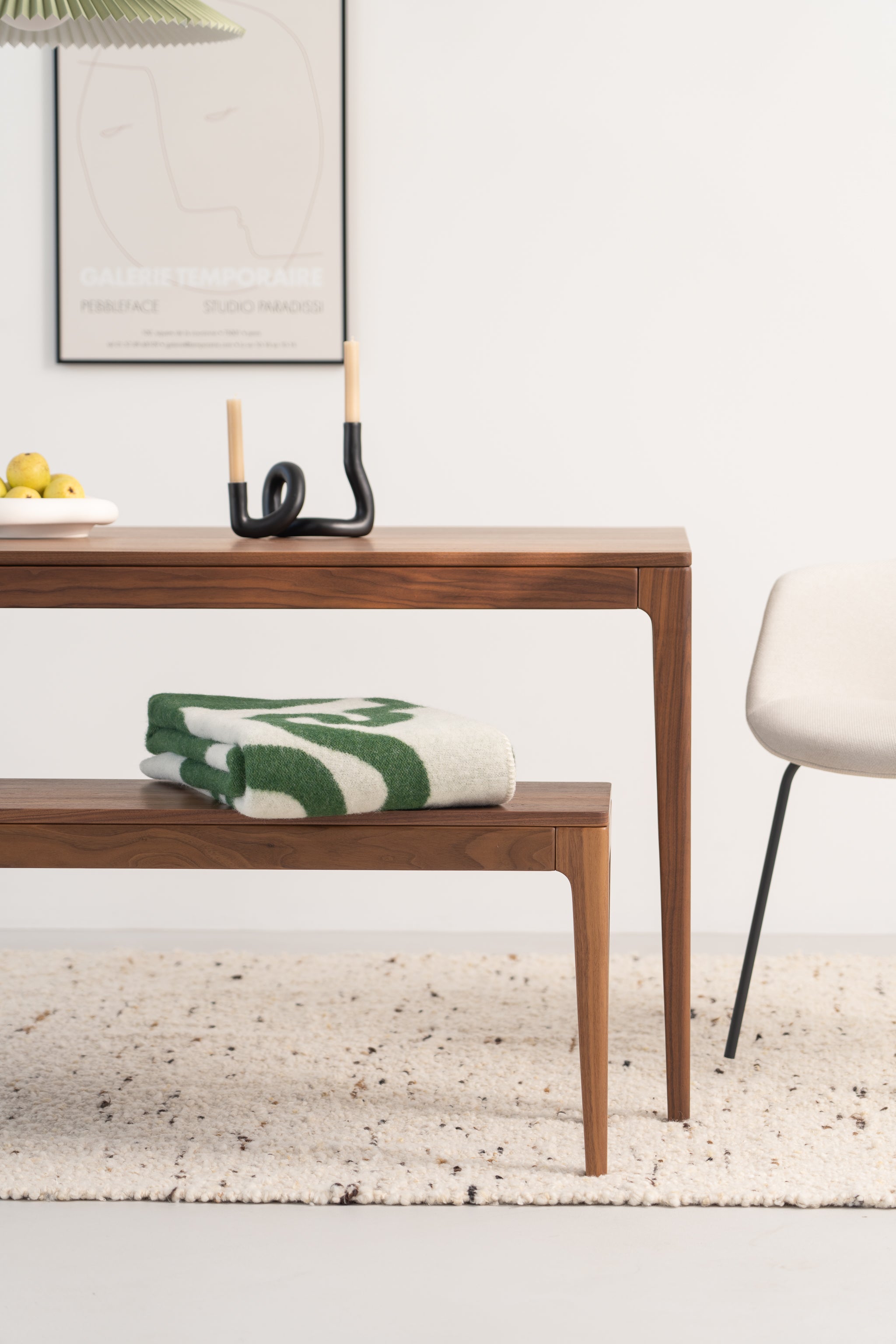 Modern dining area with wood furniture, a folded blanket, fruit bowl, unique candle holder, and minimal artwork.