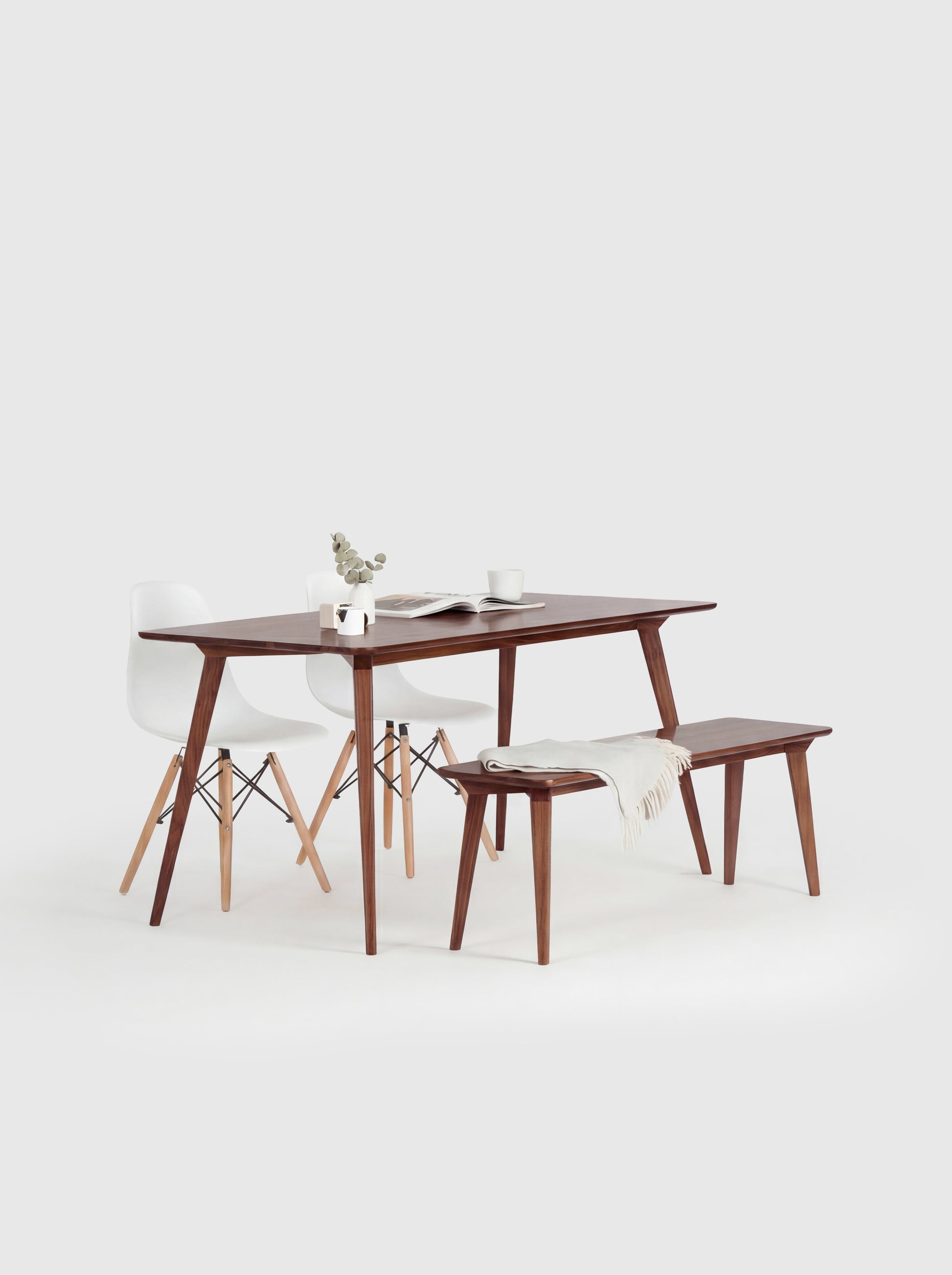 Minimalist dining set with a wooden table, bench, white chairs, and decor on a white background.