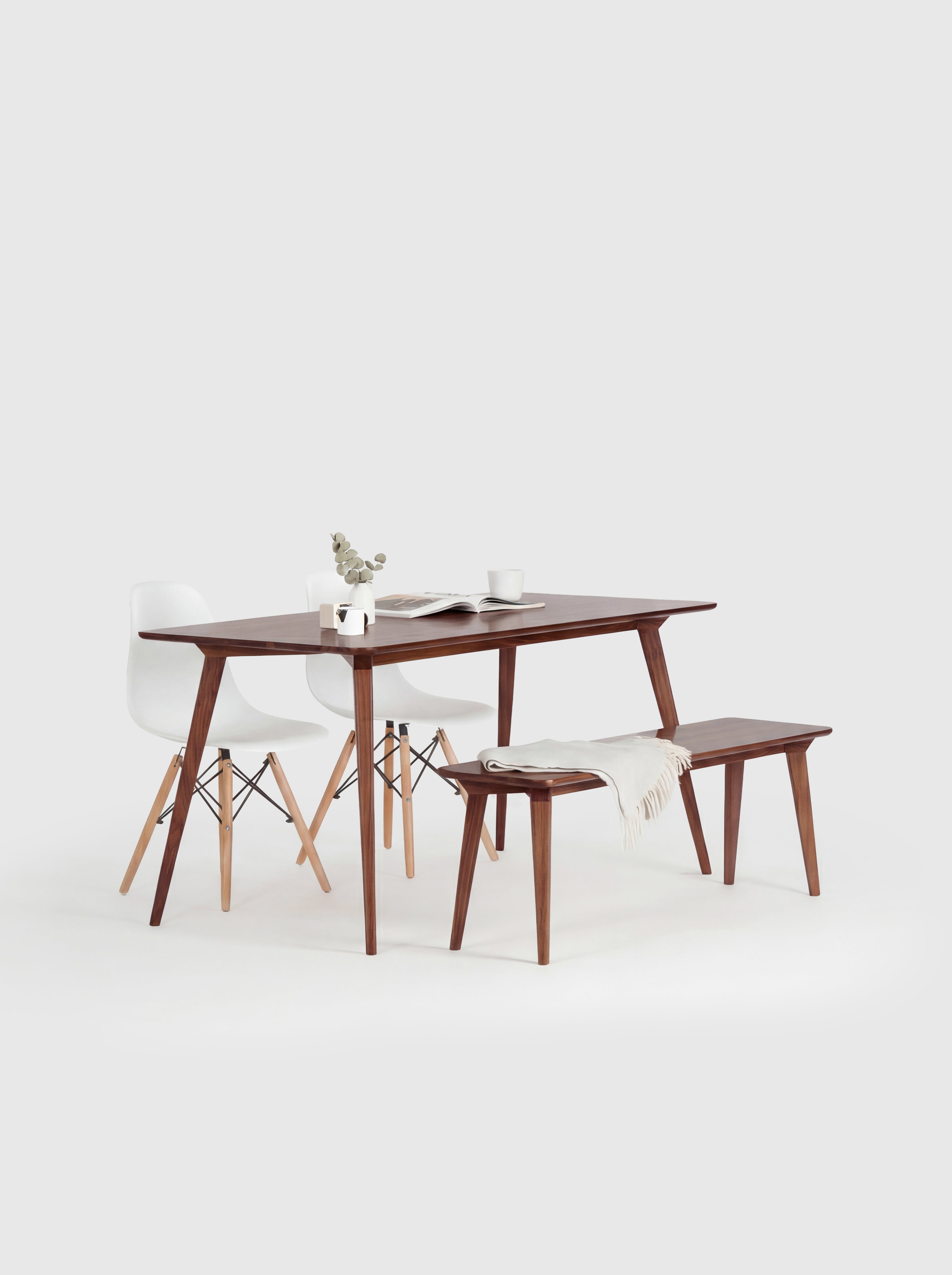 Minimalist dining set with a wooden table, bench, white chairs, and decor on a white background.