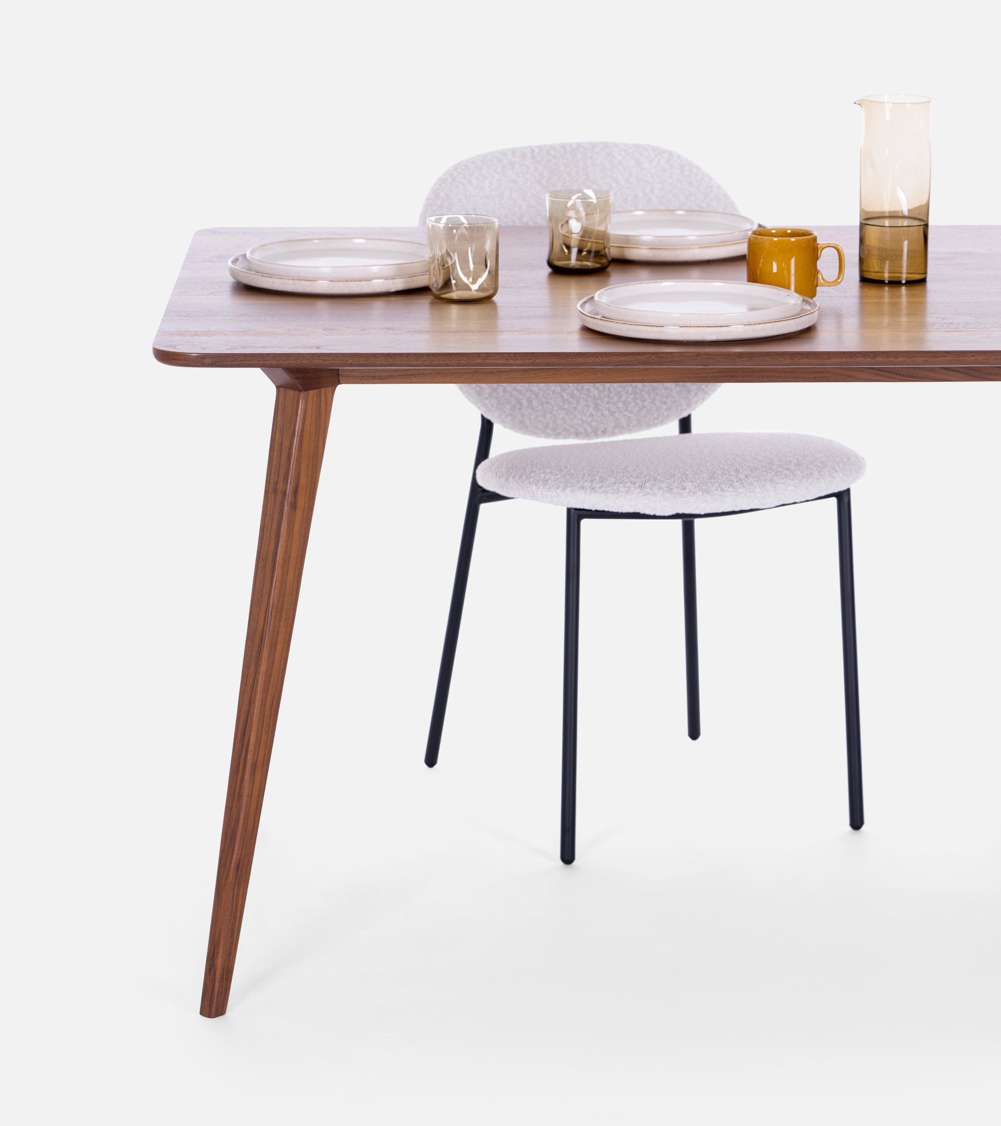Modern dining table set with two plates, glasses, a mug, and a pitcher, paired with a white chair.