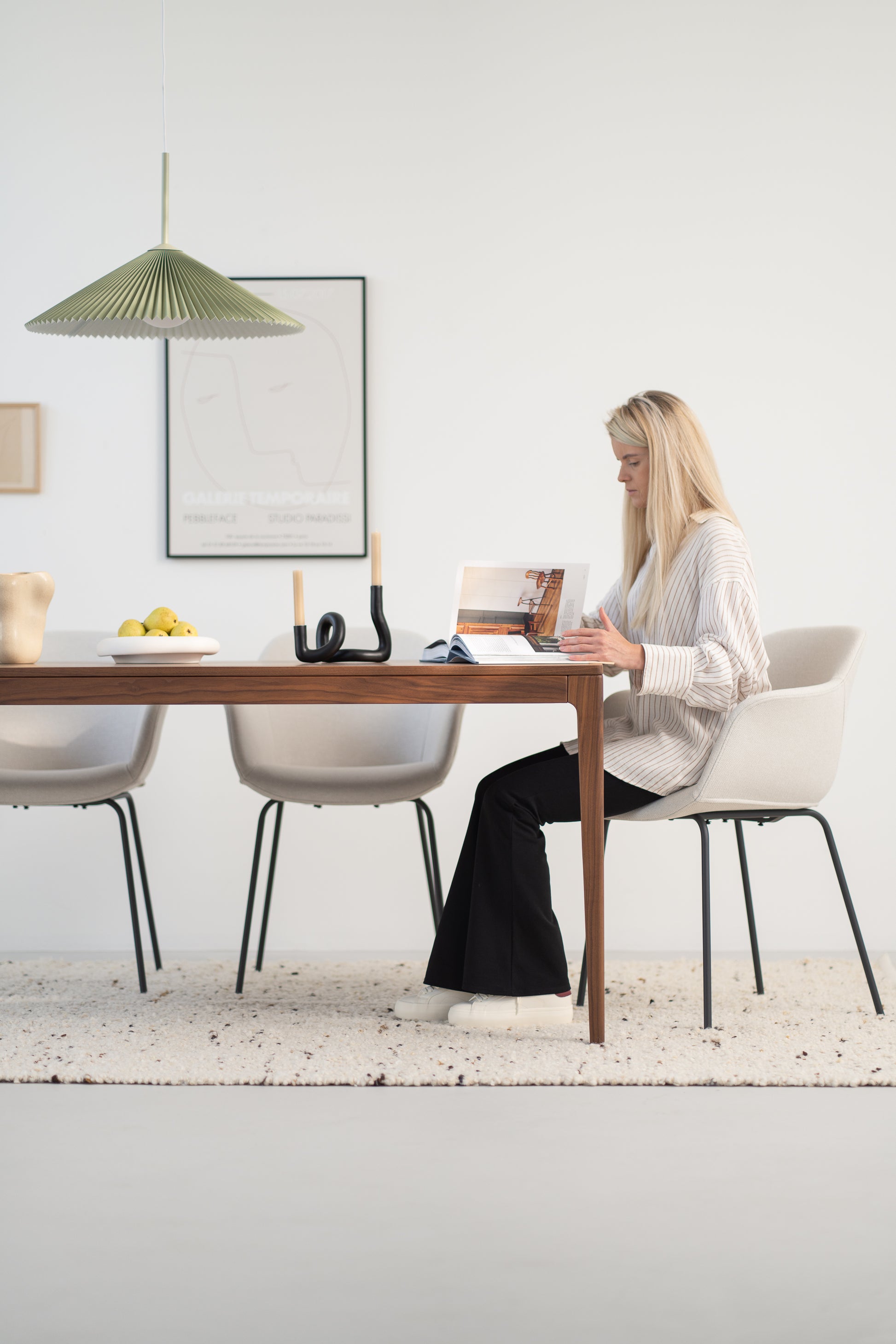 Woman reading a magazine at a modern dining table with minimalist decor.