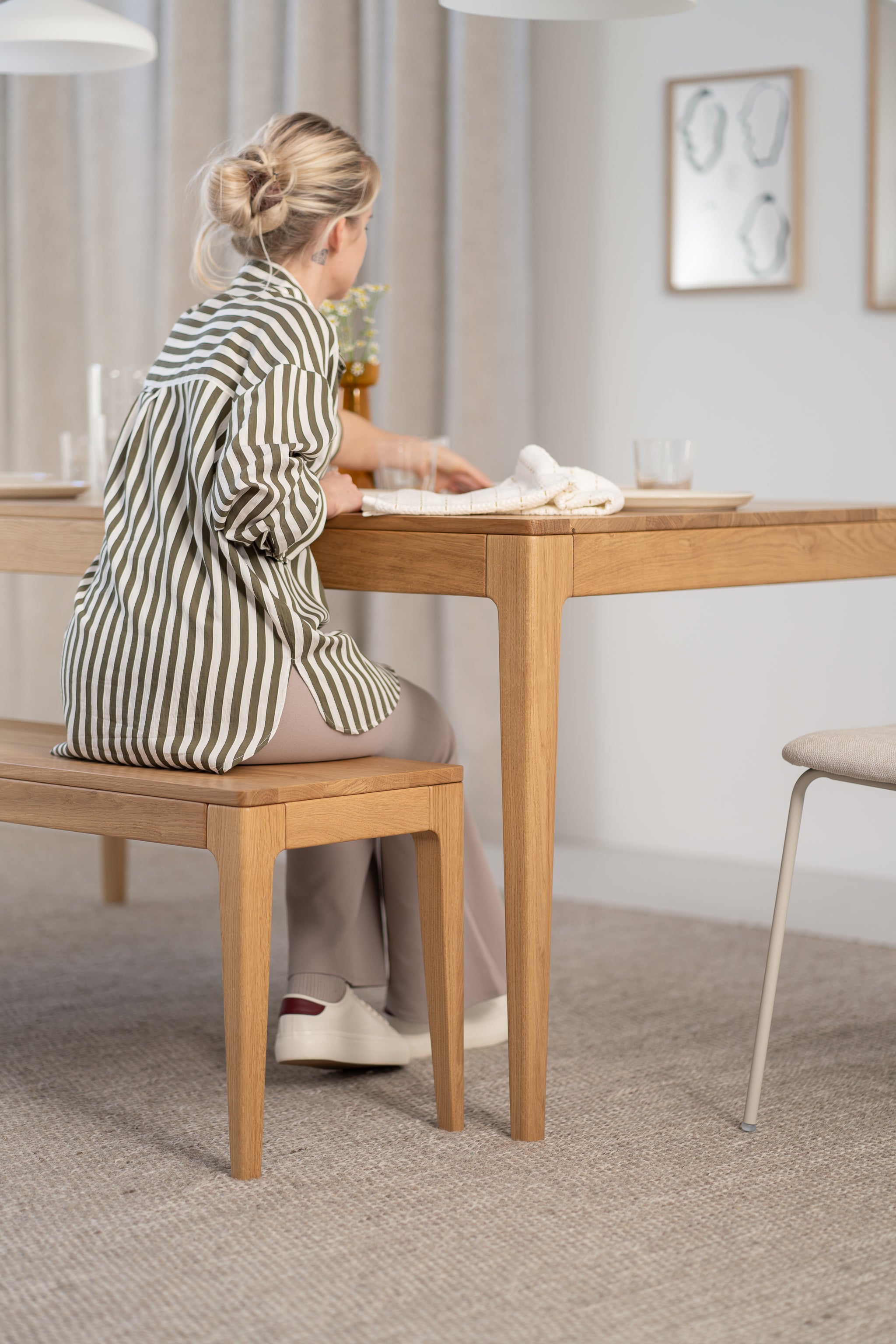 Person in a striped shirt seated at a wooden table in a modern dining room setting.