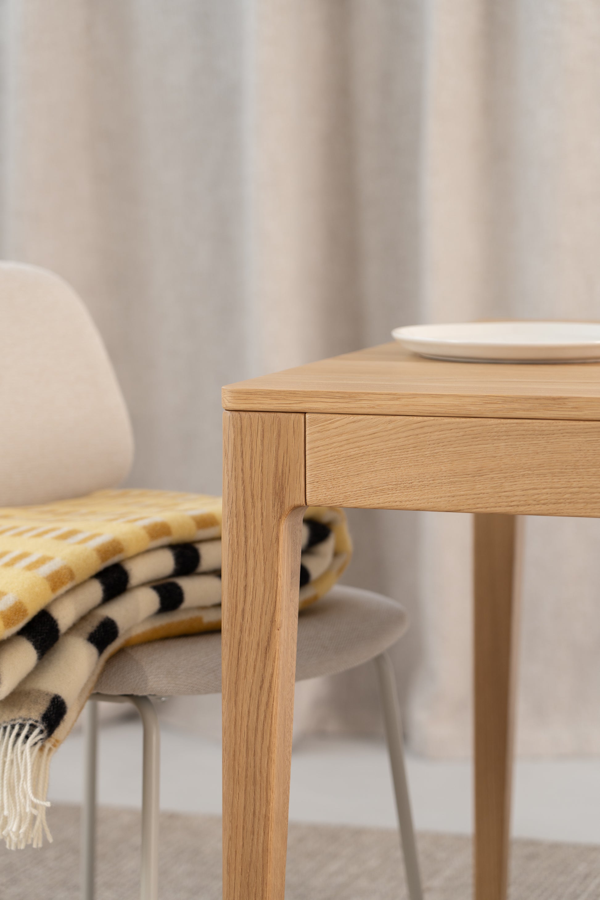 Modern wooden table with a plate, next to a chair with a patterned blanket draped over it.