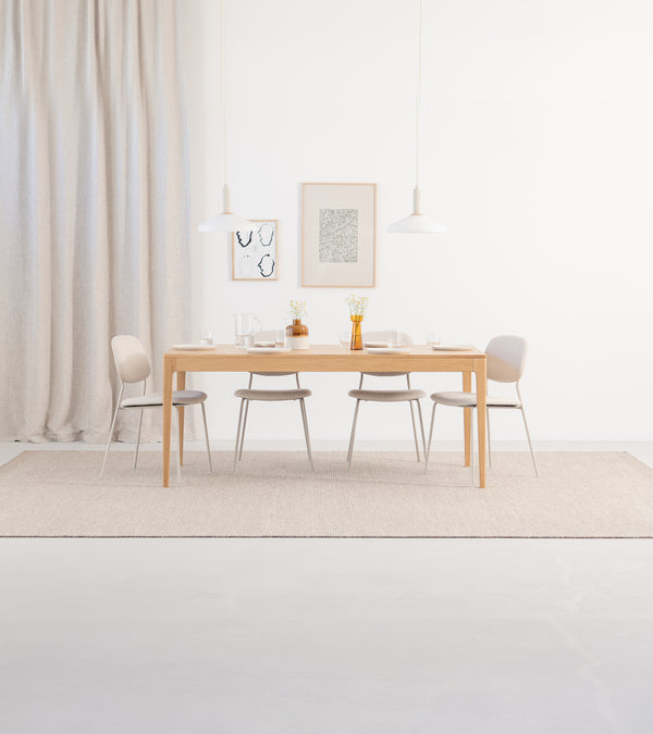 Minimalist dining room with a wooden table, four chairs, pendant lights, and wall art on a light backdrop.