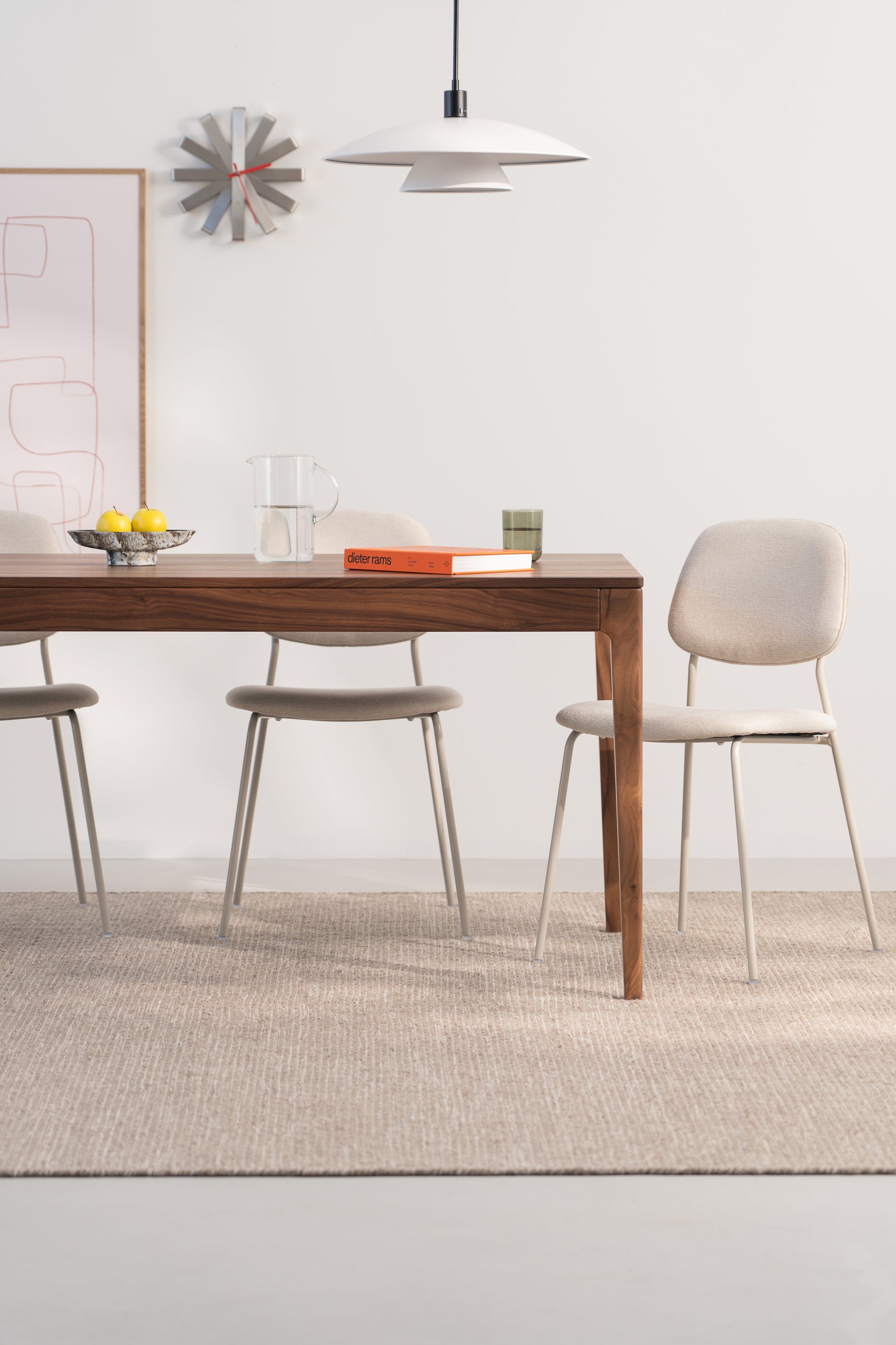 Modern dining room with wooden table, beige chairs, pendant light, wall clock, and minimalist decor.
