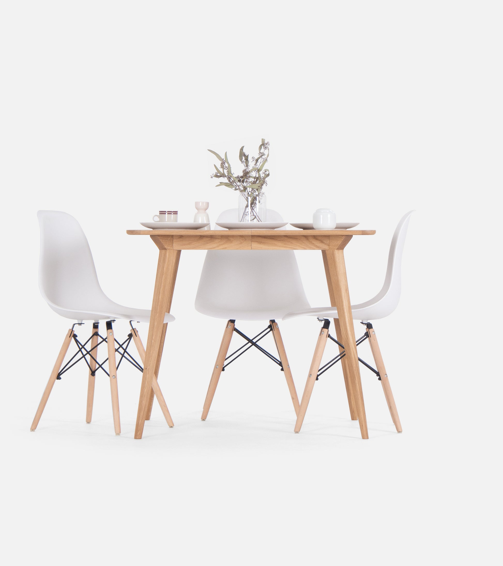 Minimalist dining set with a wooden table, two white chairs, and a vase with flowers.