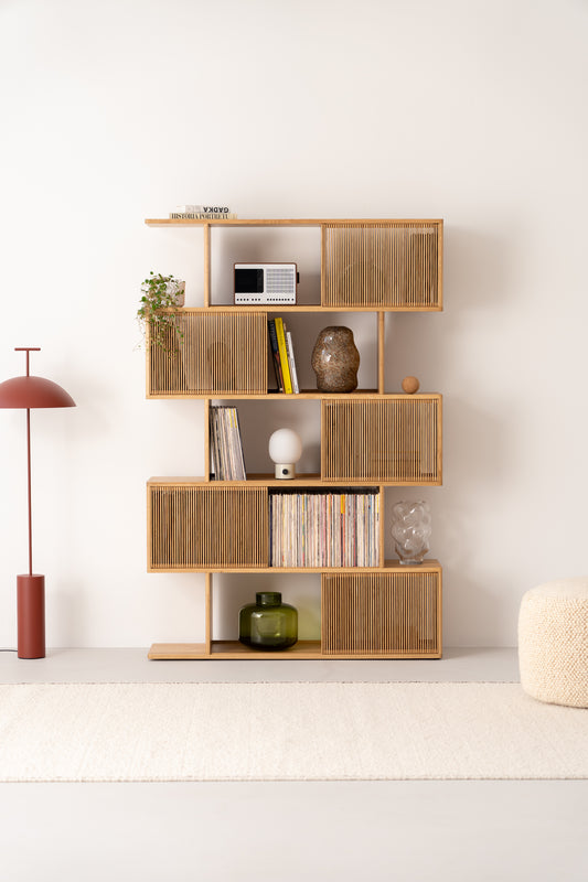 Modern wooden shelf with decor items, books, and plants. Nearby, a red floor lamp and a light ottoman on a beige rug.