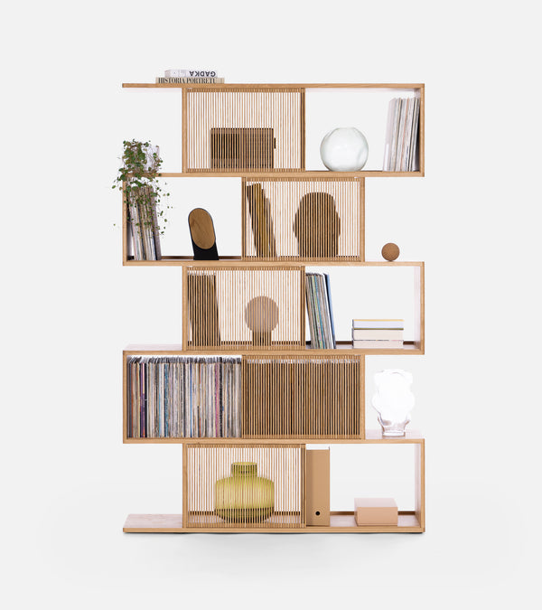 Modern wooden bookshelf with staggered shelves, books, plants, vases, and decorative items against a white background.