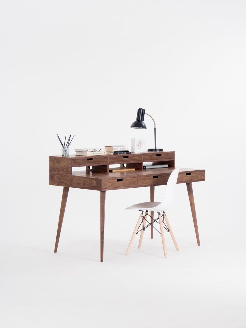 Modern wooden desk with a black lamp, books, and a white chair on a white background.