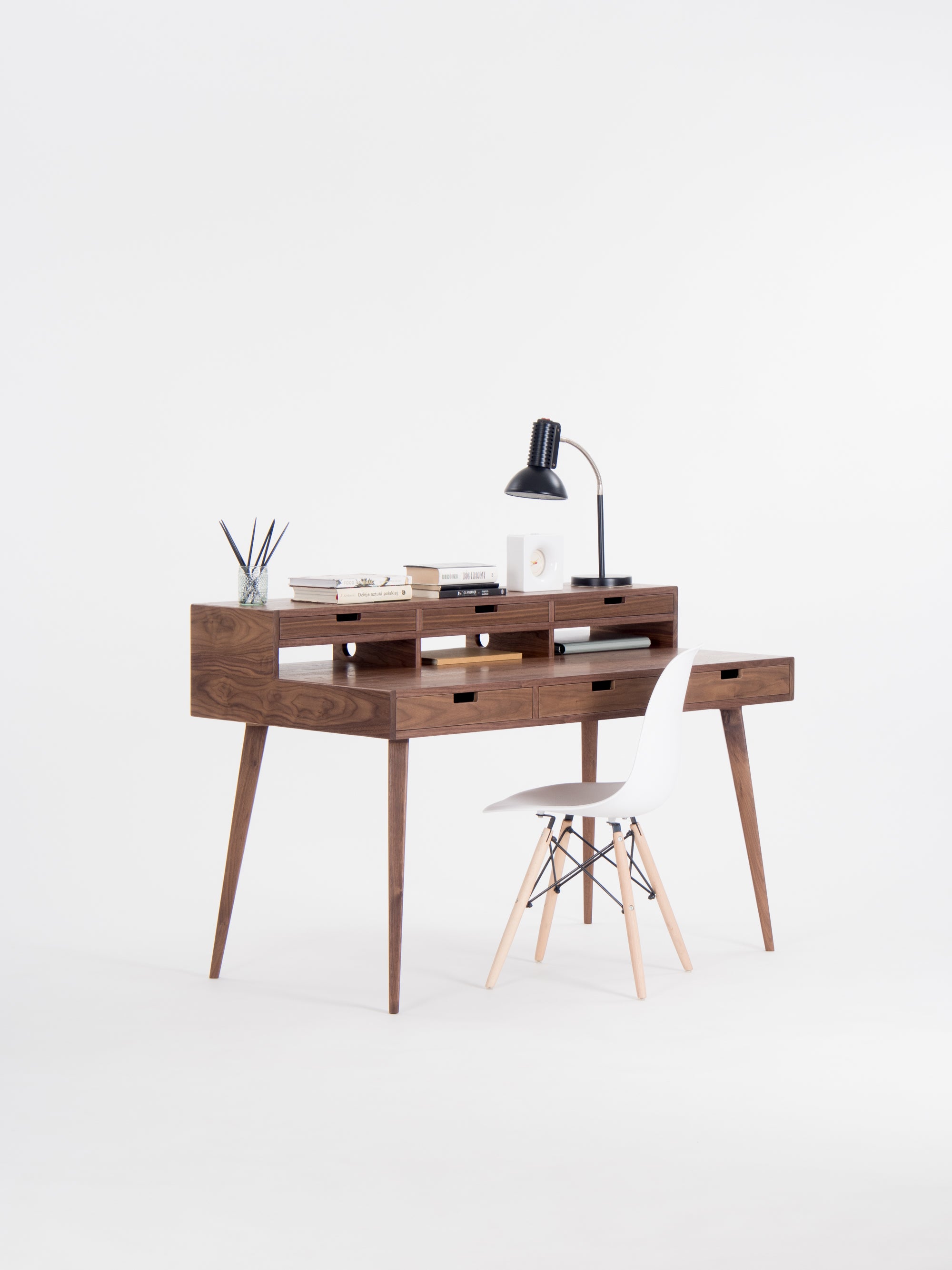 Modern wooden desk with a black lamp, books, and a white chair on a white background.
