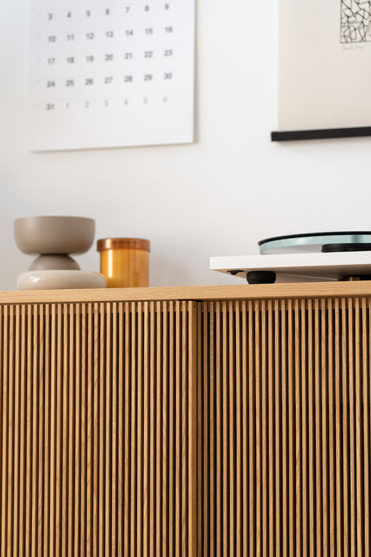 Modern wooden cabinet with decorative bowls, a candle, and a wall calendar in a minimalist room.
