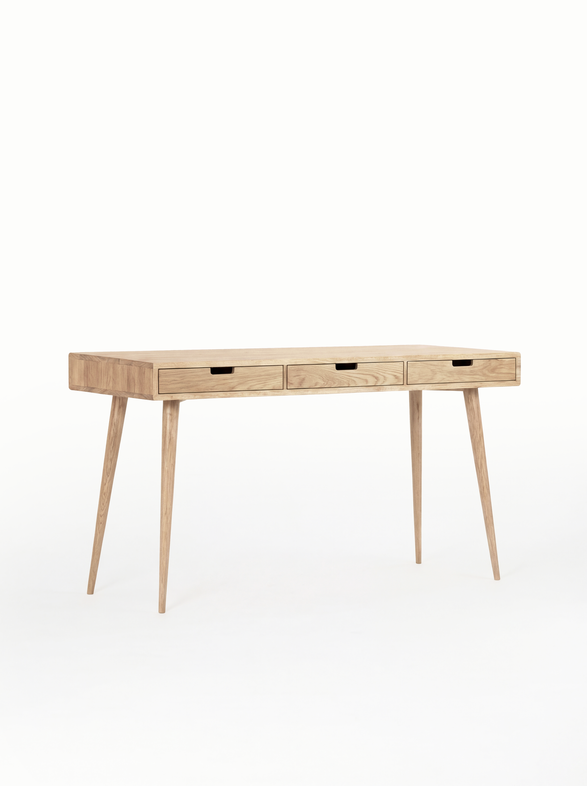 HEIM 140 narrow desk in solid oak, shown empty at an angle with three oak drawer fronts and cut-out grips