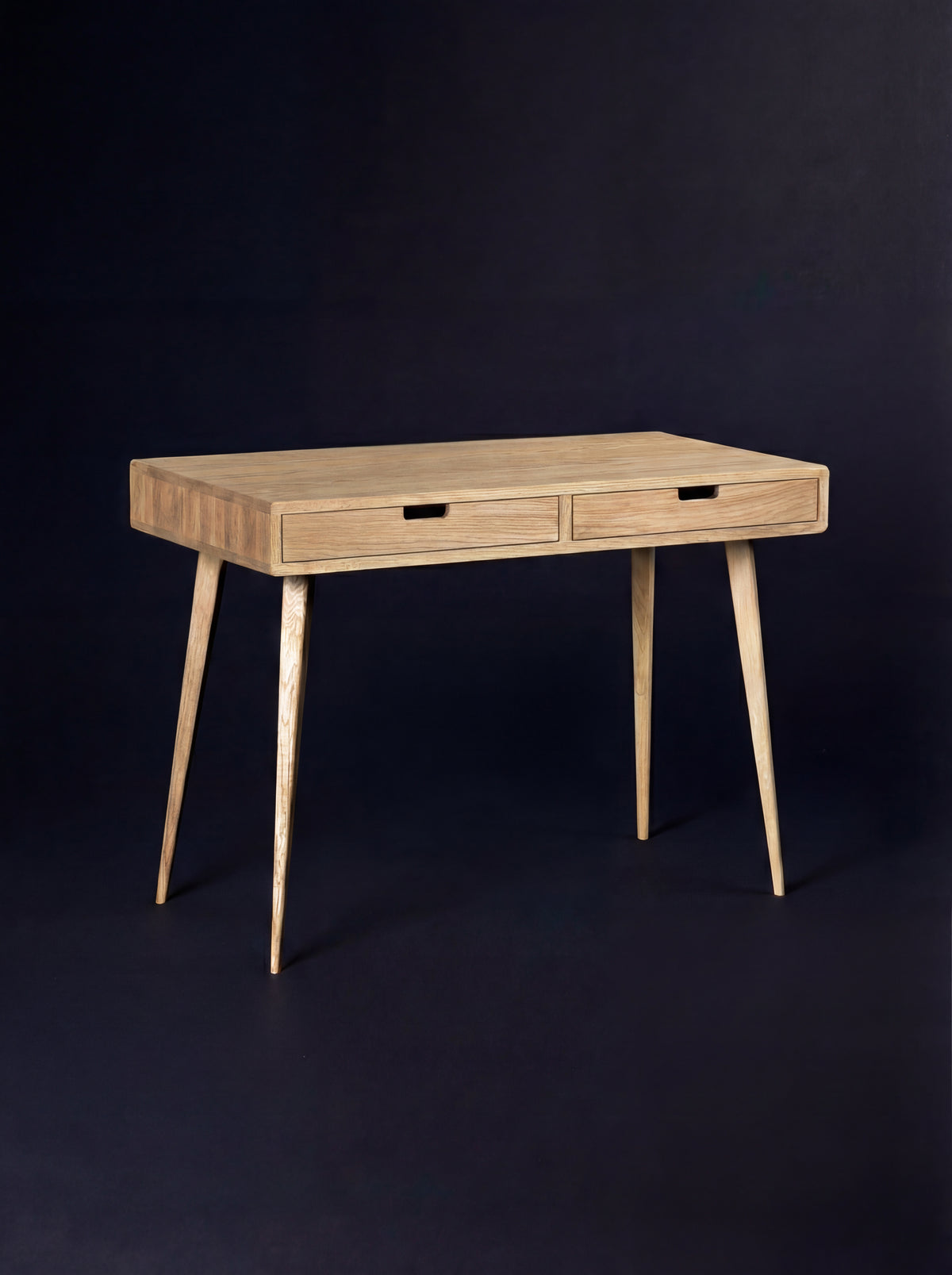 Empty HEIM 105 desk in solid oak, three-quarter view with wooden drawer fronts and splayed legs