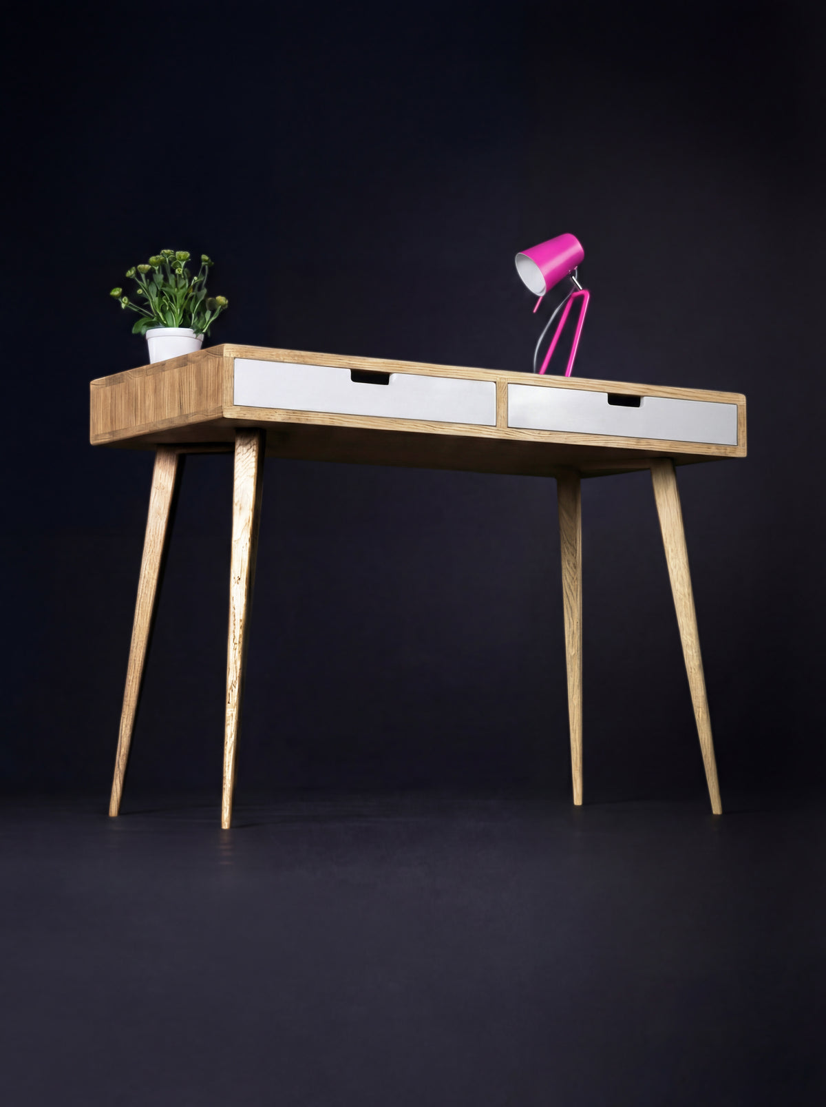 HEIM 105 desk in solid oak, angled view with two white drawer fronts, a pink lamp and a plant