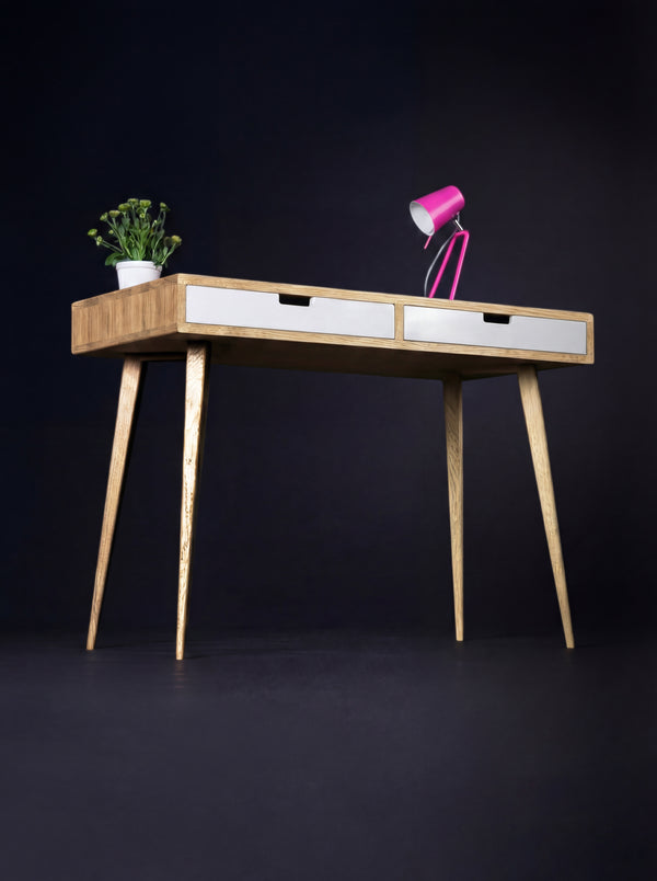 HEIM 105 desk in solid oak, angled view with two white drawer fronts, a pink lamp and a plant