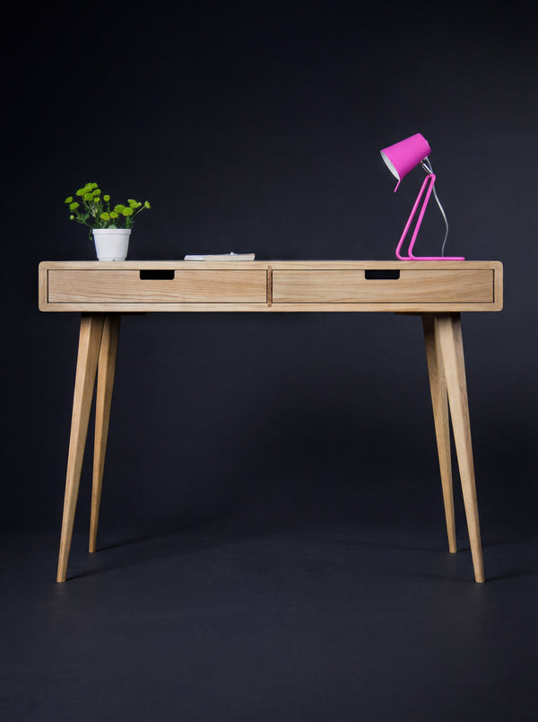 HEIM 105 solid oak desk, front view with wooden drawer fronts, a pink lamp, a plant and a thin book