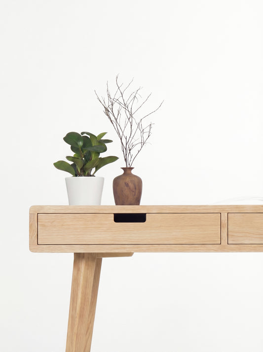 HEIM 140 desk in solid oak, left drawer front with a cut-out grip beneath a plant and a wooden vase with twigs