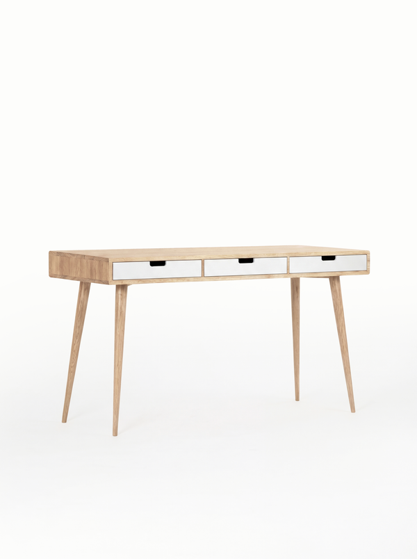 Angled view of the empty HEIM 140 desk in solid oak, with three white drawer fronts and natural oak legs