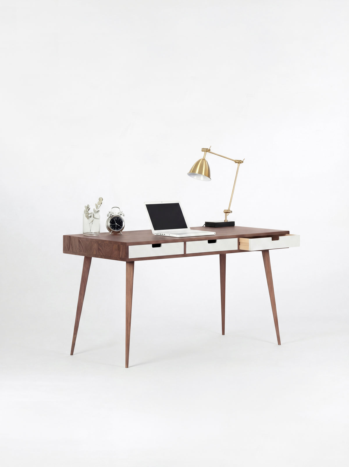 Angled view of the HEIM 140 desk in solid walnut with white drawer fronts, one drawer open and a brass lamp