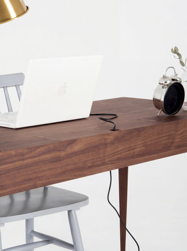 Closed cable flap on the HEIM 140 desk in solid walnut, with a laptop cable running through its notch