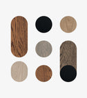 Eight wood finish swatches in circle and pill shapes on light gray, from a light oak wood color sample to jatoba and black