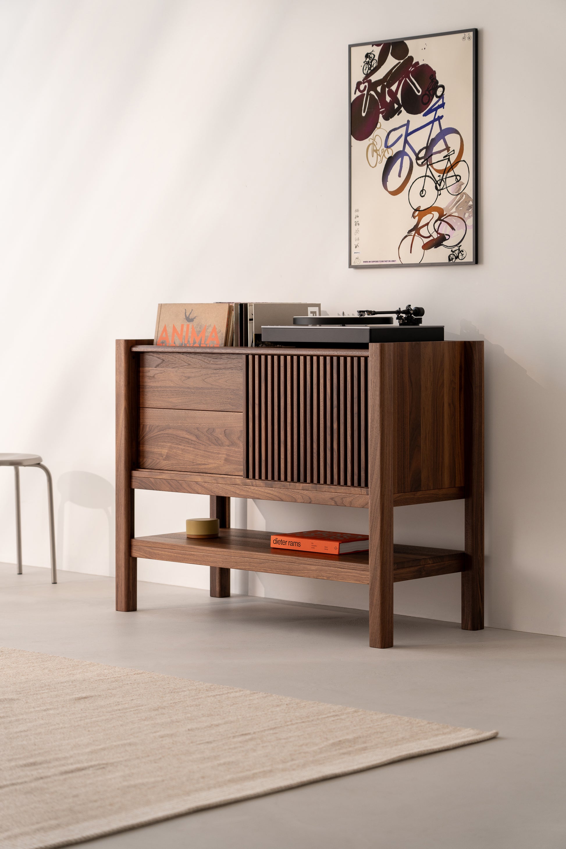Wooden cabinet with a record player, vinyls, and books, next to a wall with a bicycle art poster.