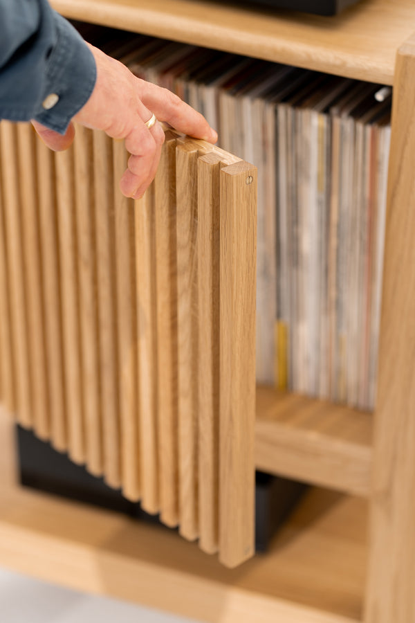 Hand opening wooden slatted cabinet door revealing a collection of vinyl records inside.